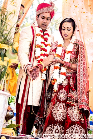 An Indian bride and groom wed under an orange mandap in a traditional Hindu ceremony. They choose a travel theme for their reception with white, blue, and pink decor.