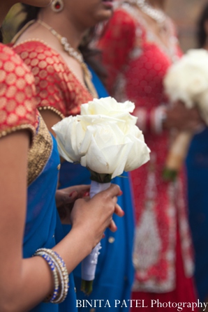 Members of the bridal party wear traditional Indian wedding clothing and carry white bouquets.