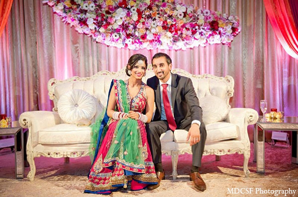 An Indian bride and groom celebrate their wedding reception after their traditional Sikh ceremony. The bride dons a colorful halter lengha and the decor has a gold and pink color palette.