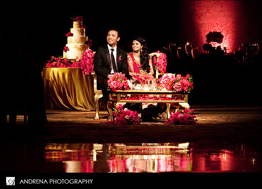 Indian bride and groom at sweetheart stage with cake behind