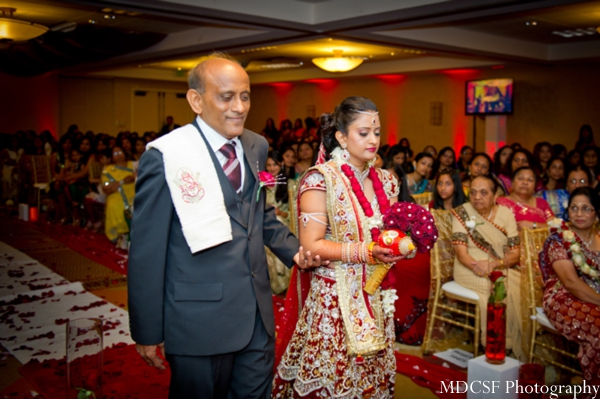 Indian bride in red and gold bridal lengha hits the aisle to her indian wedding.