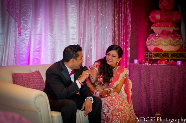 Indian bride and groom sit on pink themed Indian wedding altar.