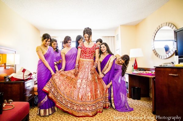 indian bride puts on red wedding lengha with bridesmaids in purple saris.