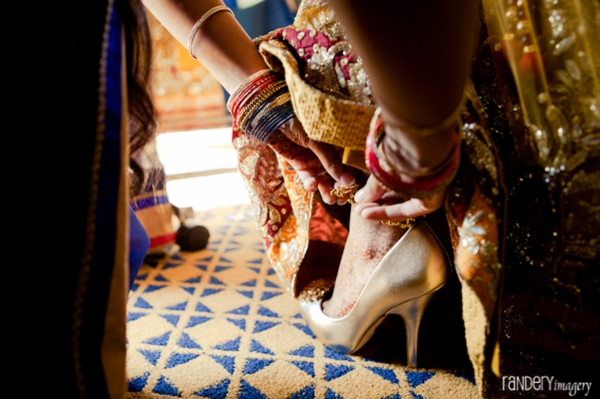 Indian bride slips on gold bridal shoes to match wedding lengha.