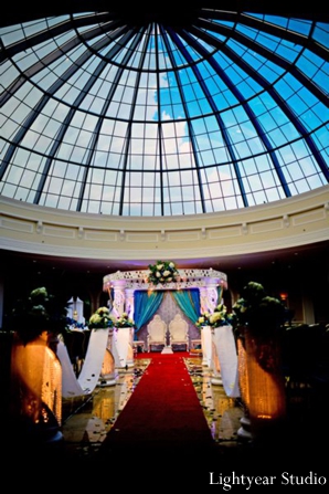 A white pillar mandap under a glass domed ceiling.