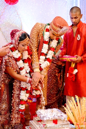 Indian bride and groom wear traditional wedding outfits and jaimala flower garlands.