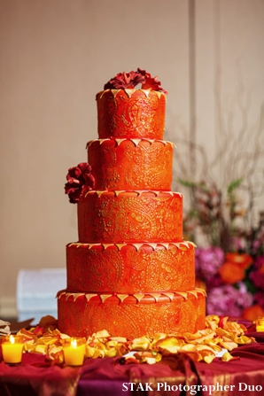 Modern Indian wedding cake in gold, orange and fresh flowers.